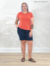 Miik model Kaitlin (5'9", xlarge) smiling wearing a navy bermuda short along with Miik's Marianna reversible neckline classic tee in papaya melange #color_papaya-melange