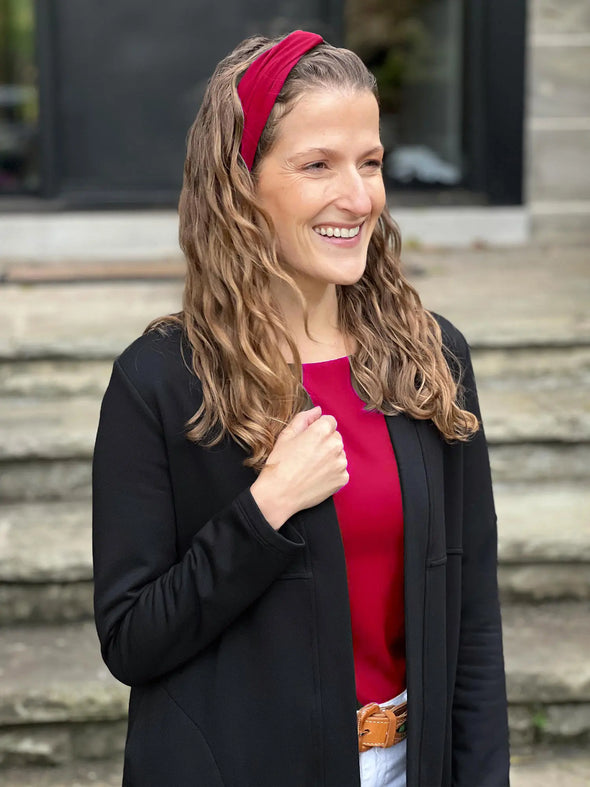 Miik model Lex smiling wearing Miik's Matana twist knot headband in cerise, with a matching colour top and a black cardigan #color_cerise 