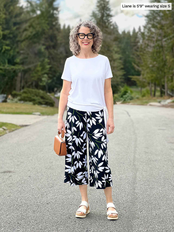 Miik model Liane (5'9", small) smiling wearing a printed capri wide leg pant with Miik's Melody side tie top in with and sandals 
#color_white 