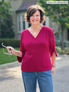 Miik founder Donna (5'6", small) smiling wearing Miik's Meron v-neck 3/4 sleeve top in cerise with jeans 
#color_cerise