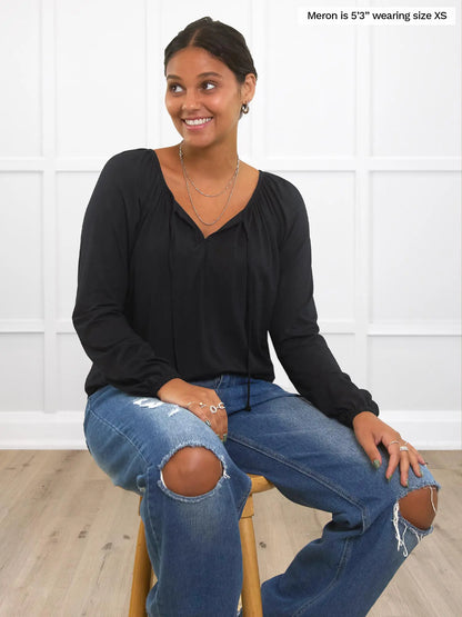 Miik model Meron (size XS) wearing the Mitchel gathered sleeve peasant blouse in black with the neck ties open, while wearing ripped jeans. 