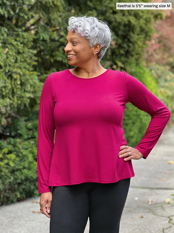 Miik model Keethai (5'5", medium) looking away wearing Miik's Pippa reversible neckline long sleeve top in cerise with a charcoal legging 