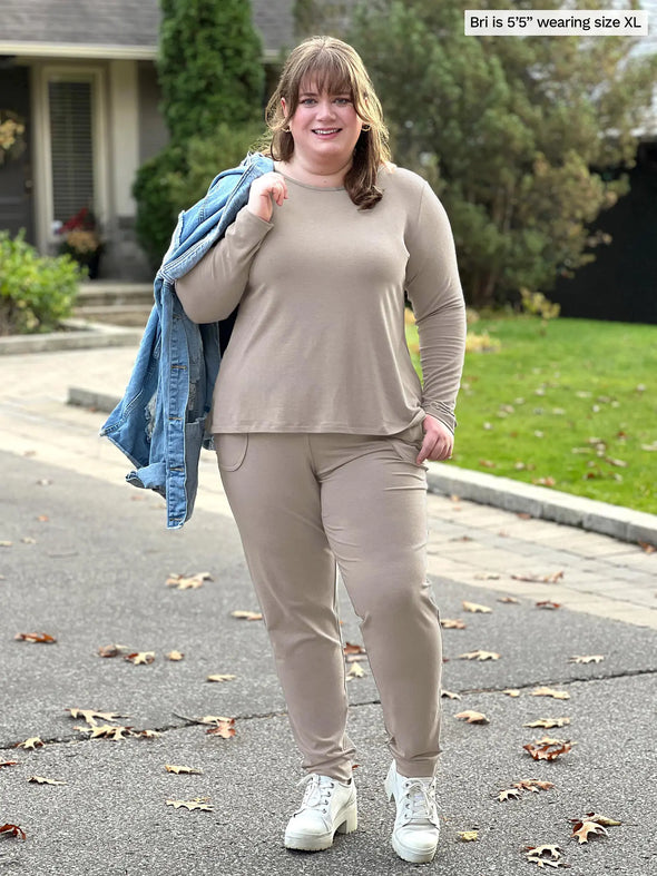 Miik model Bri (5'5", xlarge) smiling wearing a mushroom melange lounge set: Miik's Pippa reversible neckline long sleeve top and a fleece jogger with a denim jacket over her shoulders #color_mushroom-melange 