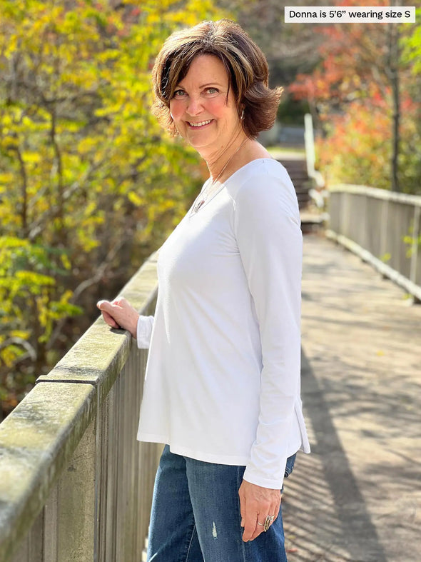 Miik founder Donna (5'6", small) smiling while standing sideway wearing Miik's Pippa reversible neckline long sleeve top in white with jeans #color_white 