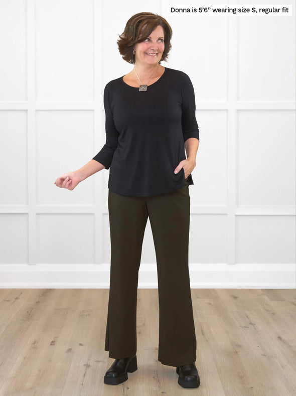 Miik founder Donna (5'6", small) smiling and looking away wearing Miik's Reed high waisted pant with pockets in olive with a long sleeve top in black and boots 
#color_olive