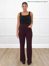 Miik model Meron (5'3", xsmall) smiling while standing in front of a white wall studio wearing Miik's Reed high waisted pant with pockets in port, regular fit, with a black tank top 
#color_port