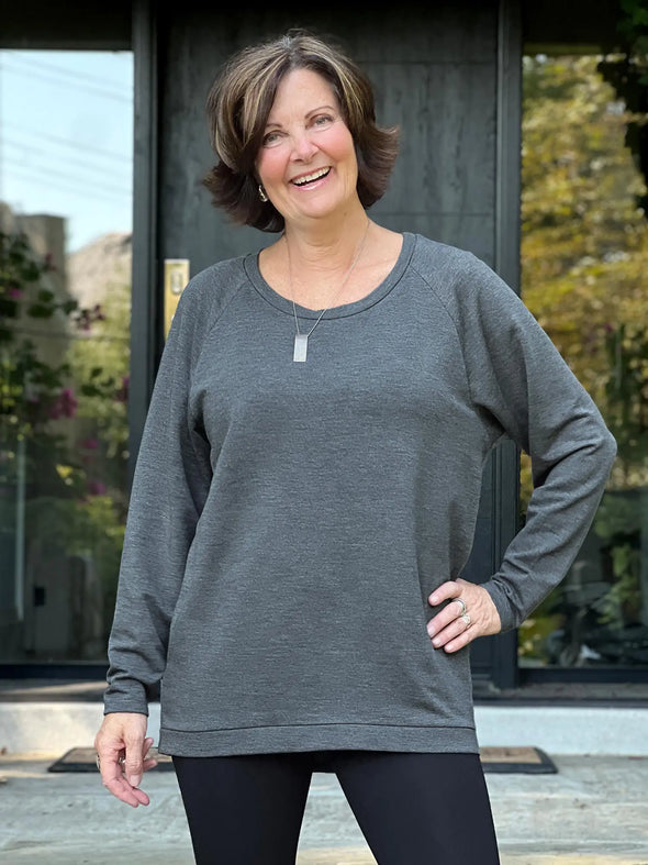 Miik founder Donna (5'6", small) smiling while standing in front of a door wearing Miik's Ria crewneck lightweight fleece sweatshirt in granite melange and leggings 
#color_granite-melange