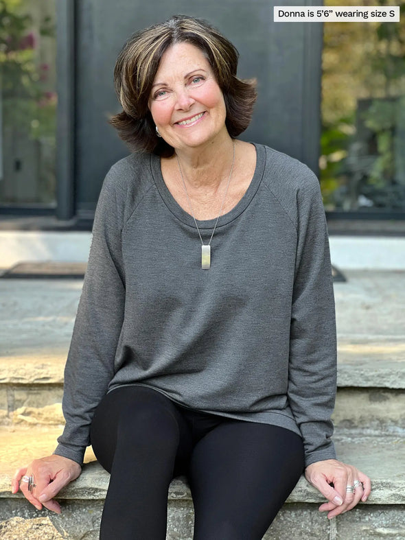 Miik founder Donna (5'6", small) smiling while sitting on a outdoor stairs wearing Miik's Ria crewneck lightweight fleece sweatshirt in granite melange and a black legging 
#color_granite-melange