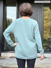 Miik founder Donna (5’6”, small) standing with her back towards the camera showing the back of Miik's Ria crewneck lightweight fleece sweatshirt in mist melange 
#color_mist-melange