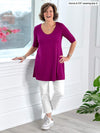 Woman standing wearing Miik's Rocelle half-sleeve scoop neck tunic in ruby pink white pants.