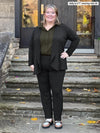 Miik model Kelly (5'7" 3x) smiling wearing Miik's Rory waterfall cardigan in black with a dress pant in the same colour and a collared shirt in olive #color_black 