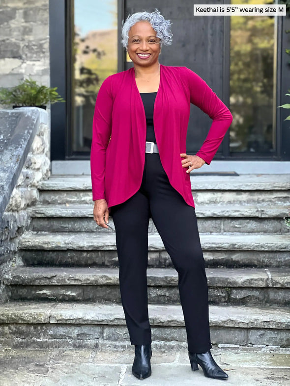 Miik model Keethai (5'5", medium) smiling wearing a black dress pant along with a tank top in the same colour and Miik's Rory waterfall cardigan in cerise
#color_cerise 