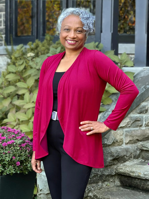 Miik model Keethai (5'5", medium) smiling wearing Miik's Rory waterfall cardigan in cerise with an all black outfit #color_cerise