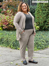 Miik model Carley (5'2", xxlarge) smiling wearing a jogger pant in mushroom melange along with Miik's Rory waterfall cardigan in the same matching colour and a charcoal tee #color_mushroom-melange 