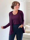 Miik founder Donna (5'6", small) smiling and looking away wearing Miik's Rory waterfall cardigan in port with a tank in the same colour and a navy high waisted pant 
#color_port