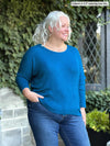 Miik model Colleen (size XXL, 5'3") wearing the Rosalie dolman sweater in moroccan blue with jeans, showing a slight side profile. 
#color_moroccan-blue