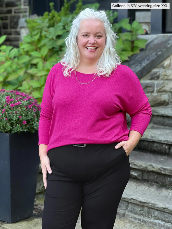 Miik model Colleen (5'3, xxlarge) smiling wearing Miik's Rosalie long sleeve dolman sweater in lipstick pink with a black dress pant 
#color_lipstick