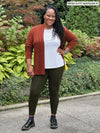 Miik model Marilyn (5'2", medium) smiling wearing a olive legging, white tee and Miik's Sadira tie waist sweater cardigan in chestnut #color_chestnut