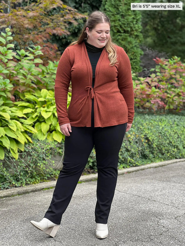 Miik model Bri (5'5", xlarge) smiling and looking down wearing an all black outfit along with Miik's Sadira tie waist sweater cardigan in chestnut #color_chestnut