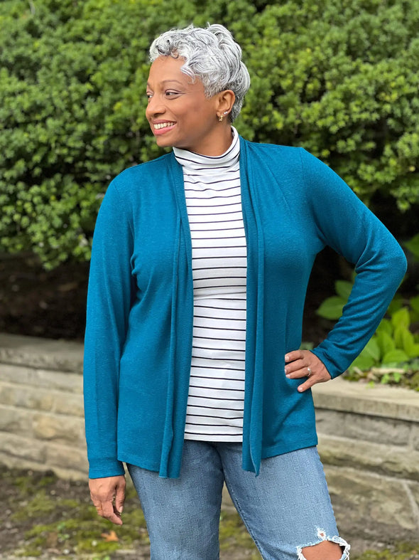 Miik model Keethai (5'5", medium) smiling and looking away wearing Miik's Sadira tie waist sweater cardigan in moroccan blue with a striped turtleneck top and ripped jeans #color_moroccan-blue