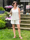 Miik founder Donna (5'6", small) smiling while standing on her backyard holding a mug wearing Miik's Sarit short PJ lounge set in grey stripe #color_grey-natural-stripe