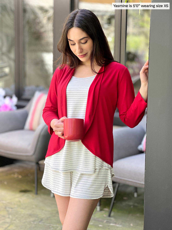 Miik model Yasmine (5'0", xsmall, petite) smiling and looking down wearing Miik's Sarit short louge set in grey stripe with a cropped cardigan in poppy red 
#color_grey-natural-stripe