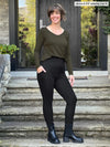 Miik model Jenna (5'9", medium) smiling wearing Miik's Seana high waisted pocket legging in black with a olive long sleeve top and black boots #color_black 