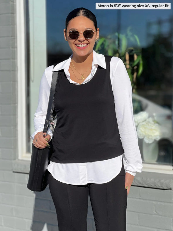 Woman standing in front of a window wearing Miik's Shandra reversible tank top in black over a white shirt and black pants.
#color_black