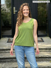 Miik model Lex (5'2", xsmall, petite) smiling and looking away wearing Miik's Shandra reversible tank top in green moss in petite fit with jeans 
#color_moss 