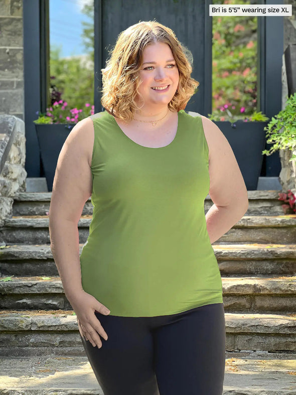 Miik model Bri (5'5", xlarge) smiling and looking away wearing Miik's Shandra reversible tank top in moss green with a black pant 
#color_moss 