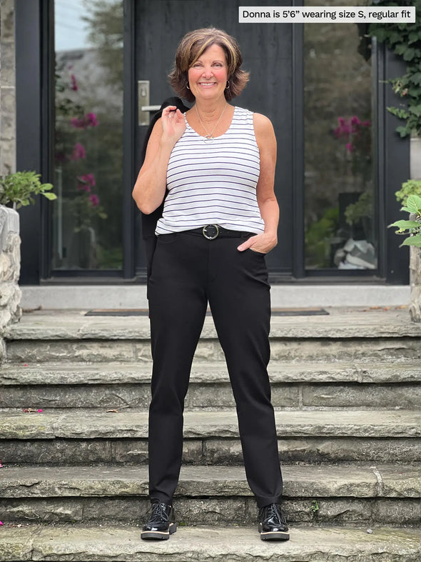 Miik founder Donna (5'6", small) smiling wearing Miik's Shandra reversible neckline tank top in newport stripe with a black dress pant and belt #color_newport-stripe