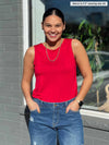 Miik model Meron (5'3", xsmall) smiling while standing in front of a window with both hands on pockets wearing Miik's Shandra reversible tank top in poppy red and jeans