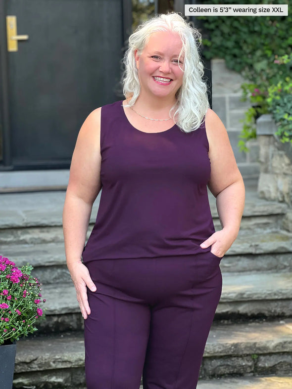 Miik model Colleen (5'3", xxlarge) smiling wearing Miik's Shandra reversible neckline tank top in port with a dress pant in the same matching colour 
#colour_port