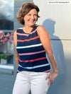 Woman standing in front of a building wearing Miik's Shandra reversible tank top in multi colour stripe and white jeans.