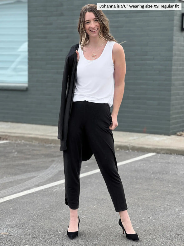 Woman standing in a parking lot smiling while wearing Miik's Shandra reversible tank top in white color with black pants.
#color_white 