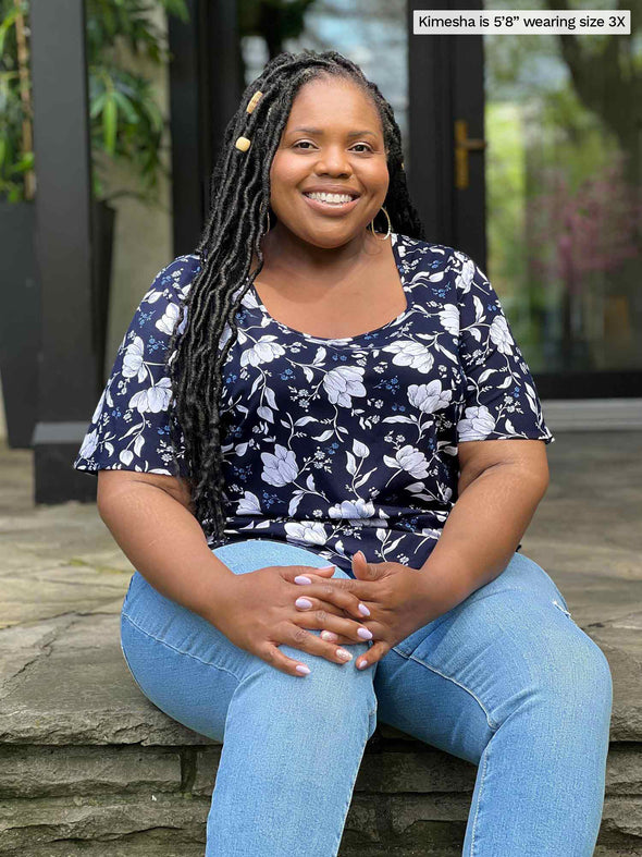 Miik model plus size Kimesha (5'8", 3x) smiling sitting on a backyard stairs wearing Miik's Shanice flutter sleeve square neck t-shirt in blossom print with jeans 
