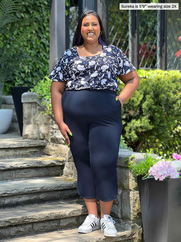 Miik model plus size Sureka (5'9", 2x) smiling wearing a capri pant in navy with Miik's Shanice flutter sleeve square neck t-shirt in blossom print