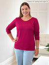 Miik model Christal 5'3", medium) smiling wearing Miik's Shannon reversible neckline long sleeve tee in cerise, regular fit, with jeans #color_cerise