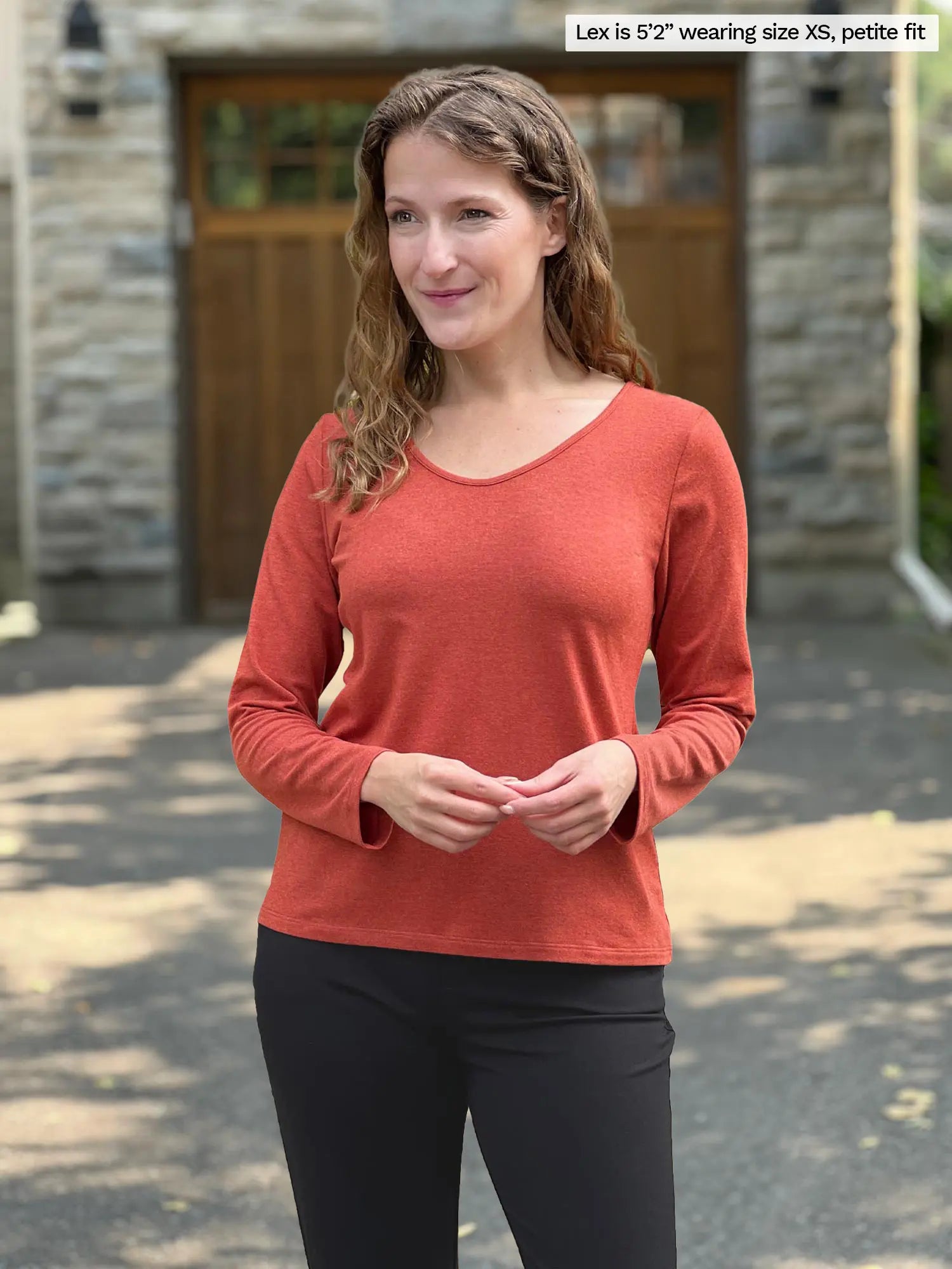 Miik model Lex (size XS) wearing the Shannon long sleeve reversible t-shirt in paprika orange, petite fit, with black pants. 