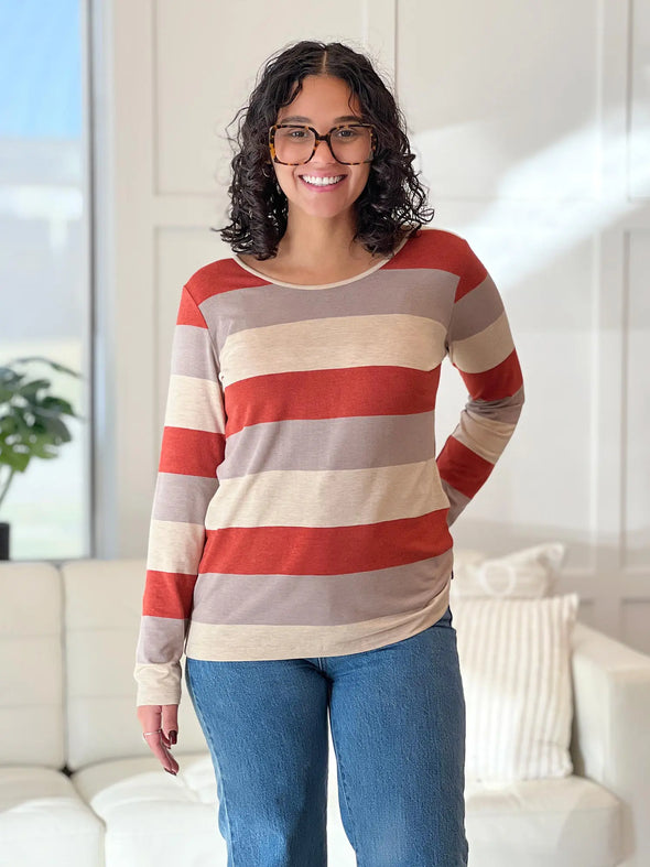 Miik model Meron (5'3", xsmall) smiling wearing Miik's Shannon reversible neckline long sleeve tee in sedona stripe with jeans #color_sedona-stripe