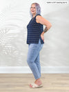 Miik model Kaitlin (5'9", xxlarge) standing sideway in front of a white wall wearing Miik's Shyanne reversible neckline side slit tank in navy pinstripe with jeans #color_navy-pinstripe 