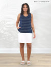 Miik model Meron (5'3", xsmall) standing in front of a white wall wearing a white skort along with Miik's Shyanne reversible neckline side slit tank in navy pinstripe #color_navy-pinstripe 