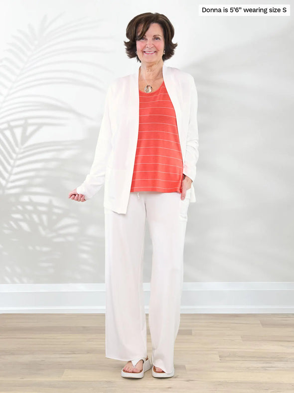 Miik founder Donna (5'6", small) smiling wearing Miik's Shyanne reversible neckline side slit tank in papaya pinstripe with a wide leg pant in natural and a cardigan in the same colour #color_papaya-pinstripe