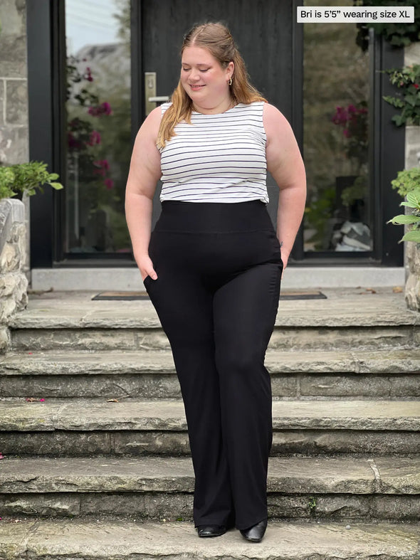 Miik model Bri (5'5", xlarge) smiling and looking down wearing Miik's Sierra high waisted pocket pant in black with a striped tank top #color_black