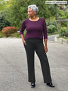 Miik model Keethai (5'5", medium) smiling and looking away wearing a port 3/4 sleeve top with Miik's Sierra high waisted pocket pant in charcoal and black boots #color_charcoal 