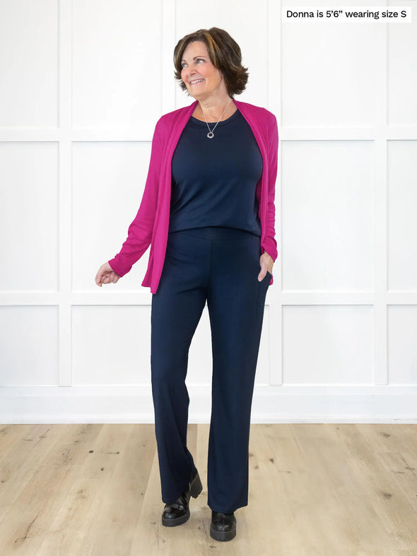 Miik founder Donna (5'6", small) smiling and looking away wearing Miik's Sierra high waisted pocket pant in navy with a matching colour top and a bright pink cardigan #color_navy