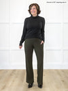 Miik founder Donna (5'6", small) smiling and looking away while standing in front of a white wall wearing Miik's Sierra high waisted pocket pant in black with a turtleneck top in black #color_olive 