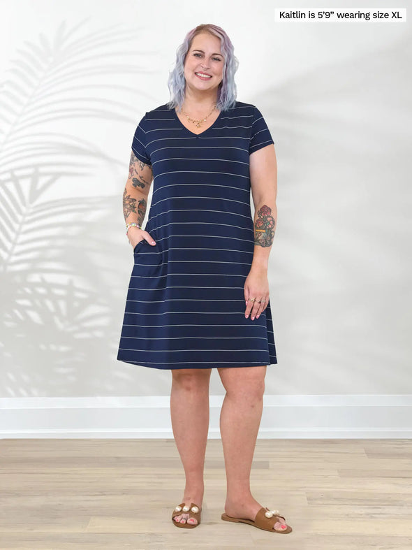 Miik model Kaitlin (5'9", xxlarge) smiling with one hand on pockets wearing Miik's Silas t-shirt dress with pockets in navy pinstripe #color_navy-pinstripe 
