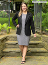 Miik model Christal (5'3", medium) smiling wearing Miik's Sofia reversible everyday dress in pebble with a washable blazer in black 