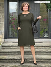 Miik founder Donna (5'6", small) smiling wearing Miik's Soraya long sleeve scoop neck pocket dress in olive with a purse and high heels #color_olive